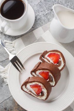 Çilek ve krem peynirle dolu çikolatalı kek rulosu. Masanın üzerinde yakın plan kahve ile servis ediliyor. Yukarıdan dikey üst görünüm