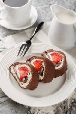 Çilek ve krem peynirle dolu çikolatalı kek rulosu. Masanın üzerinde yakın plan kahve ile servis ediliyor. Dikey