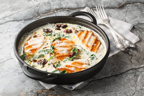 Tuscan salmon dish of grilled salmon fillet with cream sauce, garlic, sun-dried tomatoes and spinach closeup in the pan on the table. Horizonta