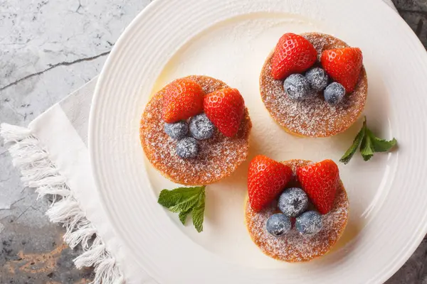 Japanese pancakes are fluffy, souffle-like pancakes that are airy perfection when topped with powdered sugar, blueberry and strawberry close-up on a plate on the table. Horizontal top view from abov