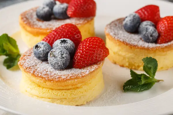 Japanese pancakes are fluffy, souffle-like pancakes that are airy perfection when topped with powdered sugar, blueberry and strawberry close-up on a plate on the table. Horizonta
