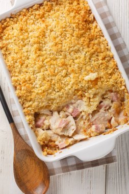 Tavuklu Cordon Bleu güveci hafif ve kremalı sosta pişirilmiş tavuk, jambon ve peynirli ekmek kırıntıları ile ahşap masadaki fırın kabına yakın. Yukarıdan dikey üst görünüm