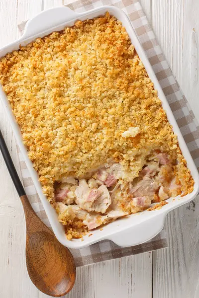 Tavuk göğsü, peynir ve jambonlu Cordon Bleu güveci beyaz ahşap masadaki fırın kabında krema kaplamasında eritildi. Yukarıdan dikey üst görünüm