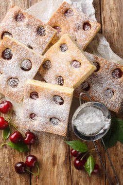 Geleneksel ev yapımı vişneli kek üzerine pudra şekeri serpiştirilmiş ahşap masanın üzerindeki parşömene yakın plan. Yukarıdan dikey üst görünüm