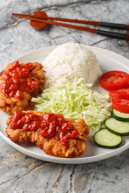 Ayam geprek terbiye edilmiş tavuk, yağda kızartılmış ve baharatlı sambal ile servis edilmiş beyaz pirinç, salatalık, domates ve lahana tabağı masanın üzerinde. Dikey