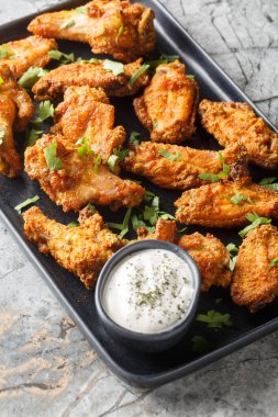 Körili çıtır tavuk kanatları, mermer masadaki tabakta Yunan yoğurdu ile servis ediliyor. Dikey