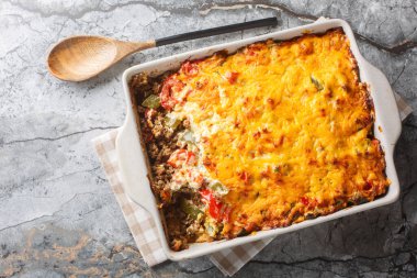 John Wayne Casserole is a delicious and filling layered casserole with taco meat, buttery biscuits, vegetables and a cheesy topping closeup on the baking dish. Horizontal top view from abov clipart