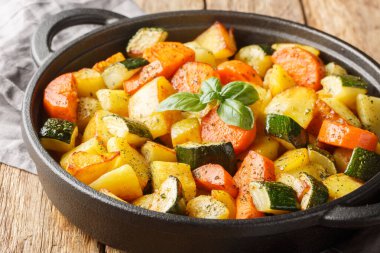 Sebzeli vejetaryen yemeği patates, havuç, kabak ve sarımsak, ahşap bir masada kızartma tavasında. Yatay