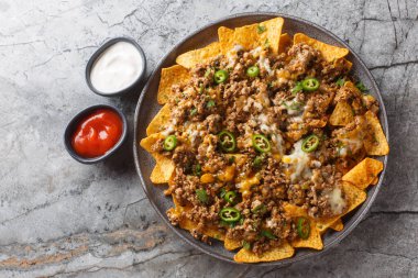 Mısır cipsi ve bol miktarda kıyma, çedar peyniri ve biberli biber. Masanın üzerindeki tabağa yakın soslar servis ediliyor. Yukarıdan yatay üst görünüm