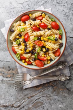 Masadaki tabakta taze fusilli makarna salatası, siyah fasulye, domates ve mısırın yakın çekimi. Yukarıdan dikey üst görünüm