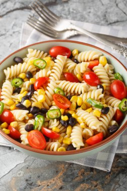 Masadaki tabakta taze fusilli makarna salatası, siyah fasulye, domates ve mısırın yakın çekimi. Dikey
