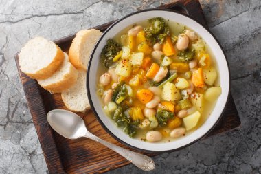 Fasulye, patates, balkabağı, lahana, havuç, soğan ve kereviz karışımlı sebze çorbası masanın üstünde. Yukarıdan yatay üst görünüm