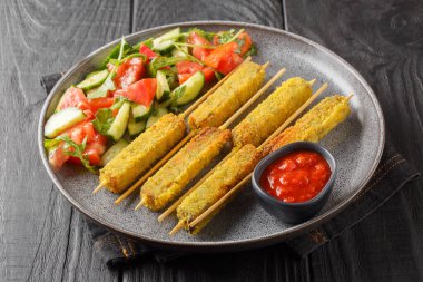 Sebzeli salata ve domates sosuyla servis edilmiş vejetaryen kebaplı patlıcan. Tahta masadaki tabağa yakın plan. Yatay