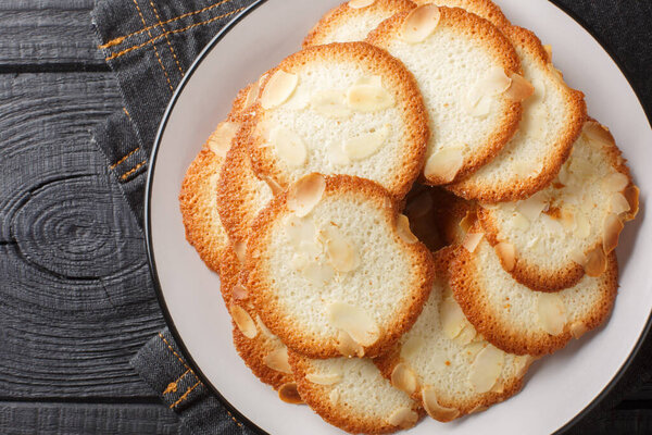 Almond tuiles Tejas de almendras, roof tile shaped almond pastry closeup on the plate on the table. Horizontal top view from abov