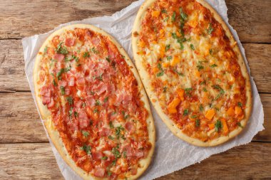 Pinsa Romana pizza with cheese, ham and tomato sauce close-up on parchment on wooden table. Horizontal top view from abov clipart