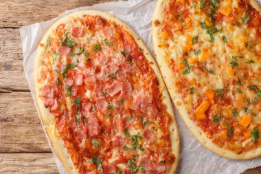 Delicious Roman pizza with cheese, ham and tomato sauce close-up on parchment on wooden table. Horizontal top view from abov clipart