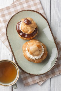 Dini hamur işi iki choux çöreğinden oluşur. Pasta kremayla doldurulur, üzeri çikolata ganache ile kaplanır ve ahşap masadaki krema kaplaması ile süslenir. Yukarıdan dikey üst görünüm
