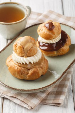 Dini hamur işi iki choux çöreğinden oluşur. Pasta kremayla doldurulur, üzeri çikolata ganache ile kaplanır ve ahşap masadaki krema kaplaması ile süslenir. Dikey