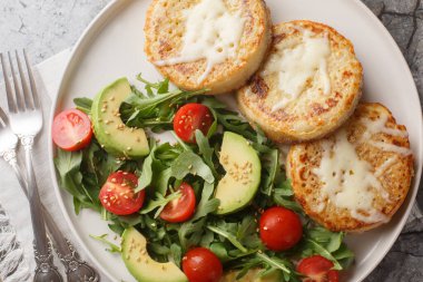 Cheesy Eggy Crumpets with salad made of avocado, tomato, arugula and spinach closeup on the plate on the table. Horizontal top view from abov clipart