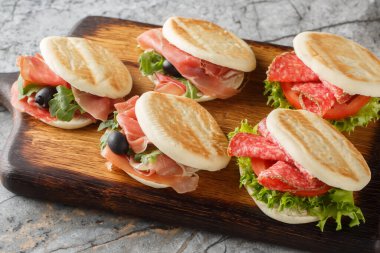 Small italian tigelle sandwiches with sausage, jamon and fresh vegetables close-up on wooden board on table. Horizonta clipart