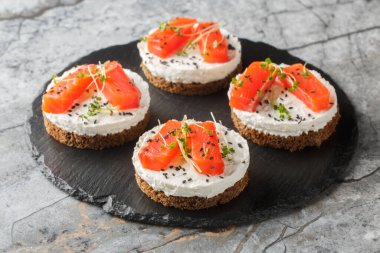 Sağlıklı peynirli sandviçler, kırmızı balıklı, krem peynirli, susamlı ve mikroyeşillikli masaya yakın plan. Yatay