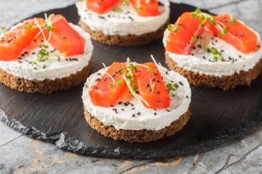 Sağlıklı kahvaltı, krem peynirli somonlu çavdar ekmekli sandviç, masada susam ve mikro yeşillikler. Yatay