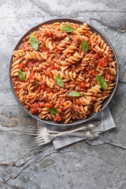 Italian Big Fusilloni bolognese pasta with a beef tomato sauce closeup on the plate on the table. Vertical top view from abov clipart