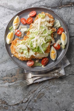 Ekmekli tavuk göğsü, yumurta, parmesan, buzdağı marulu ve domatesli salata. Masanın üstünde. Yukarıdan dikey üst görünüm