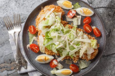 Delicious fresh schnitzel caesar salad with chicken meat, eggs, parmesan, iceberg lettuce and tomatoes close-up in a plate on the table. Horizontal top view from abov clipart