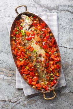 Caribbean stew of whole sea fish with vegetables close-up in a frying pan on the table. Vertical top view from abov clipart