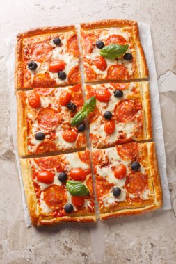 Salamlı, zeytinli, mozzarella peynirli ve domates soslu sıcak börek pizzası masadaki parşömen kağıdına yakın plan. Yukarıdan dikey üst görünüm