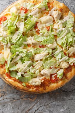 Sezarella soslu pizza, tavuklu fileto, buzdağı salatası yaprakları ve masadaki ahşap tahtaya yakın plan parmesan peyniri. Yukarıdan dikey üst görünüm