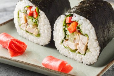 Delicious sushi burrito with rice, chicken, cream cheese, vegetables, nori and lettuce close-up in a plate on the table. horizonta clipart