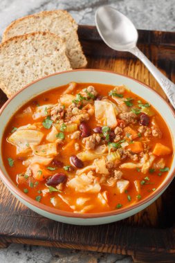 Masadaki tabakta kırmızı fasulye, soğan, domates, havuç ve kereviz yakın plan lahana çorbası. Dikey