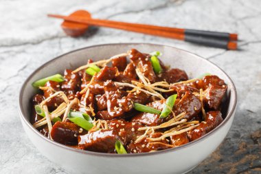 Hafif tatlı soslu kızarmış zencefilli biftek, yeşil soğan ve masanın üzerindeki kasede susamlı yakın çekim. Yatay