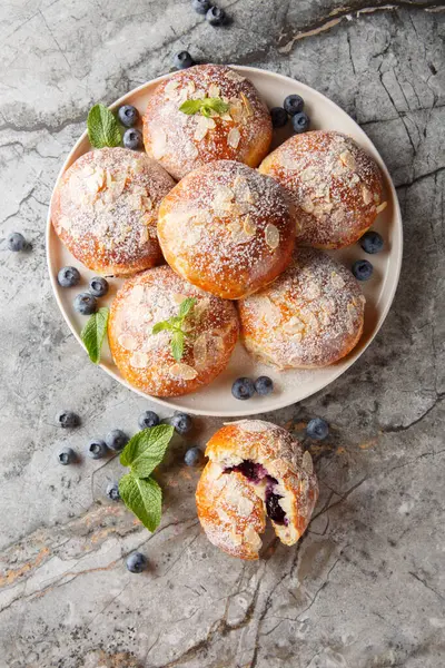 Brioche çörekleri, yaban mersini, badem gevreği ve pudra şekerini masaya yakın plan çek. Yukarıdan dikey üst görünüm
