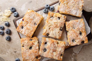 Yaban mersinli kahvaltı keki taze böğürtlenlerle dolup taşıyor ve üzerine de masadaki tahta tahtaya yakın kıymık dilimlenmiş bademler konuyor. Yukarıdan yatay üst görünüm