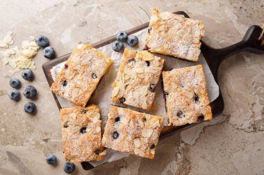 Masadaki tahtanın üzerindeki her ısırıkta fındıklı badem tadında yaban mersinli kek ve sulu yaban mersini. Yukarıdan yatay üst görünüm