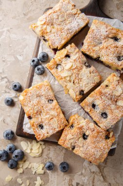 Yaban mersinli badem turtası ekstra nemli, yumuşak, yabanmersiniyle dolu ve masadaki tahta tahtaya yakın bademlerin güzelliğine sahip. Yukarıdan dikey üst görünüm