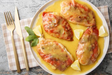 Bir tavuklu saltimbocca prosciutto kaplı tavuk, çıtır çıtır adaçayı ve masanın üzerindeki tabağa yakın duran limonlu beyaz şarap sosu içerir. Yukarıdan yatay üst görünüm