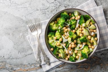 close-up of a dietary salad of broccoli, chickpeas, avocado, onion, and parsley in a bowl on a table. Horizontal top view from abov