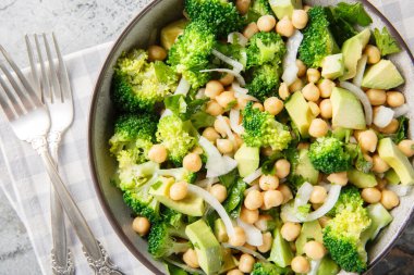 green salad of broccoli, chickpeas, avocado, onion, and parsley with lemon oil, close-up in a bowl on a table. Horizontal top view from abov