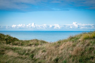 landscape background with dunes water sea and blue sky and white clouds