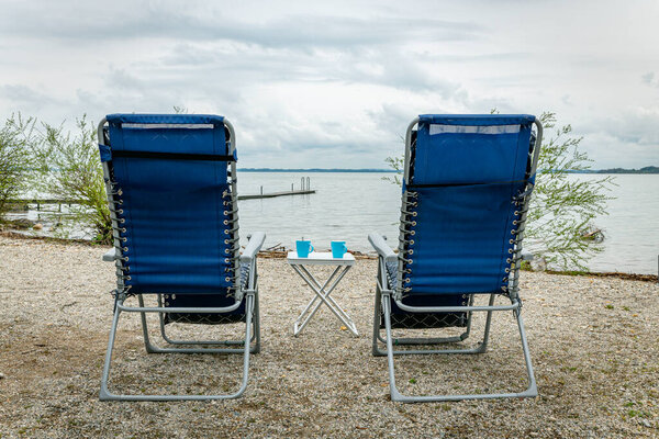 two blue adjustable garden chairs at a table with two cups of coffee overlooking the chiemsee in Germany