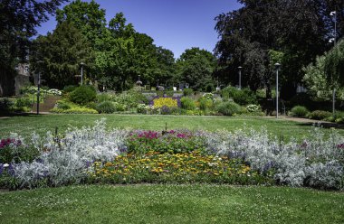Çimenli güzel bir İngiliz Bahçesi, yeşil ağaçlı sınırlar ve mor turuncu renkli çiçekler, süslemeli bir yükseklik.
