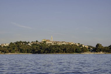 Hırvatistan 'ın liman kenti Vrsar, C' den gelen bir teknede görüldü. Evlerde güneş vardı ve ormanın ortasında, kasabanın üzerinde yükselen kilise vardı.