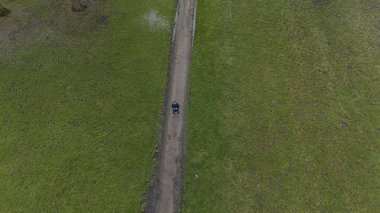 İnsansız hava aracı ya da insansız hava aracı uçuran bir adamın yeşil bir arazide çimenli bir iz üzerinde durduğu görüntüsü.