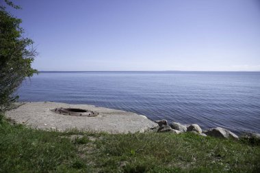 the blue water of the kattegat at trelde naes in denmark with blue water and sky and with The Foundation of metal on concrete of the old cannon. clipart