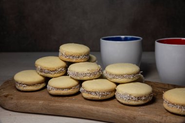 Ahşap bir tahtada hindistan cevizli kurabiye yığını. Yanında da iki seramik kahve fincanı. Tatlıdan zevk almak için rahat bir ortam yaratıyor..