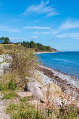 Sakin mavi suları, çakıllı plajı ve berrak gökyüzünün altındaki yemyeşil bitki örtüsüyle sakin bir sahil manzarası büyüleyici. Danimarka 'da barış ve doğal güzelliğin mükemmel bir temsili.